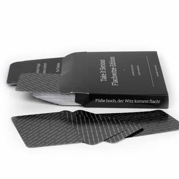 Spielkarten liegen neben der Spielverpackung Take It Serious Flachwitze-Edition