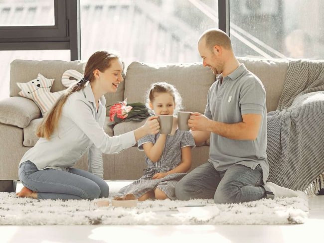 Familie sitzt auf dem Teppich im Wohnzimmer